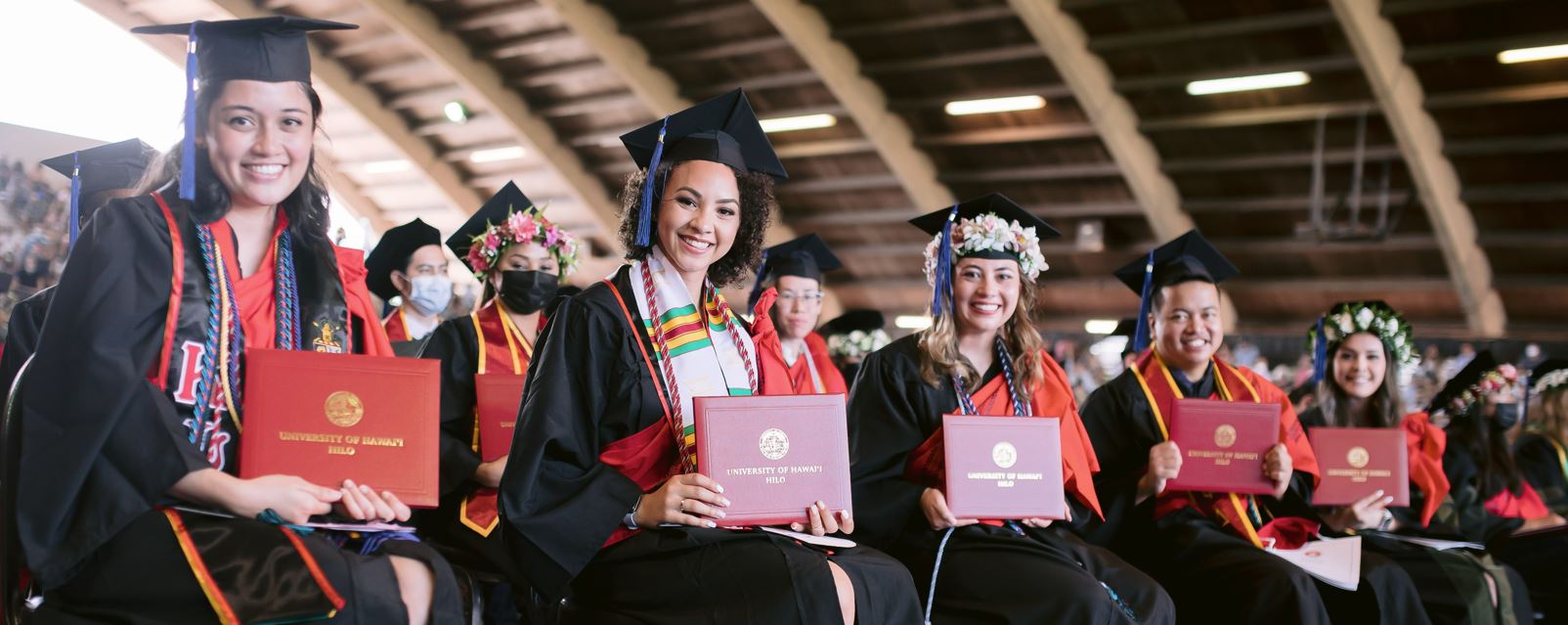 Smiling graduates seated at a commencement ceremony show their UH Hilo diplomas