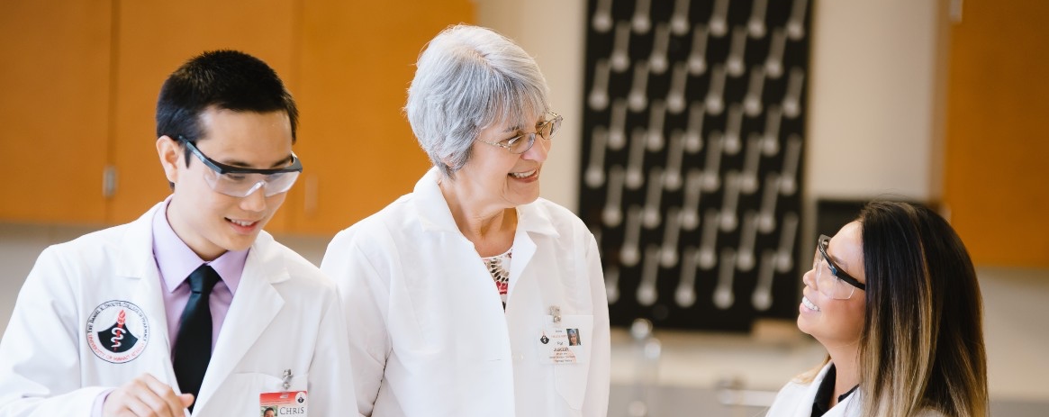 A professor works with two students in a lab.