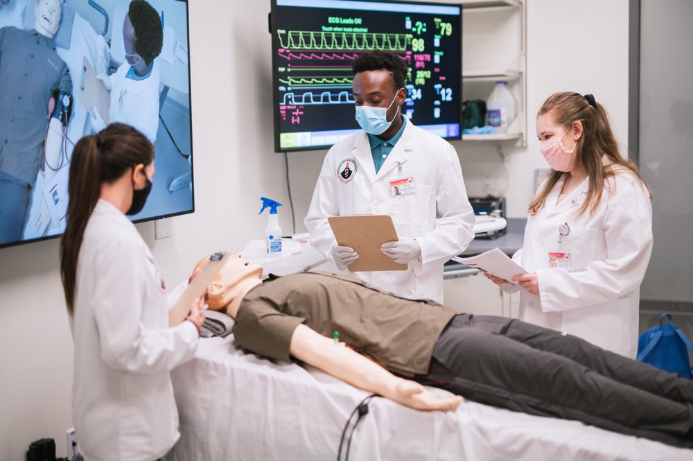 Three students learn on a simulation mannequin in a mock hospital setting