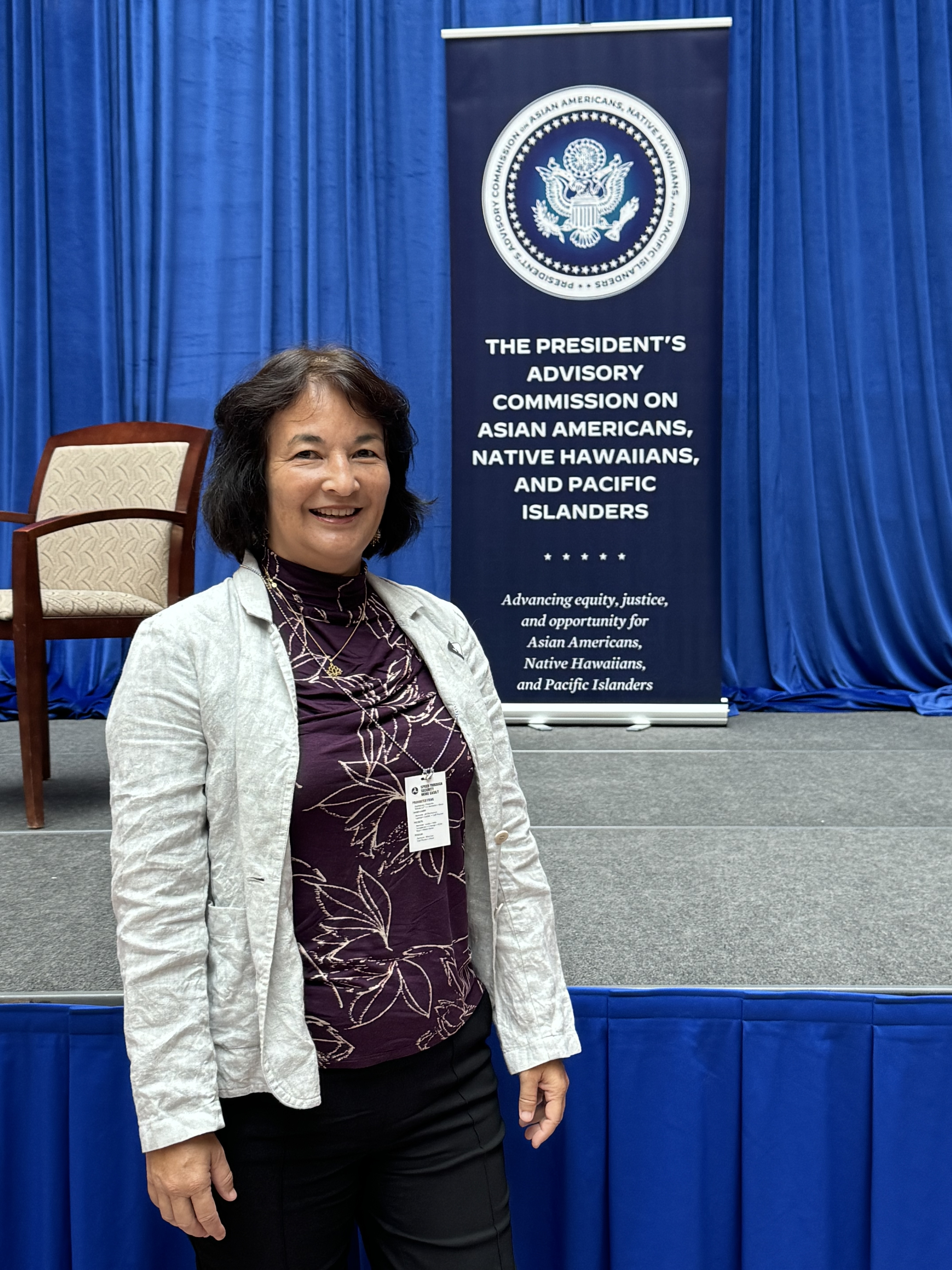 Dr. Taira stands in front of a sign that reads "President's Advisory Commission on Asian American, Native Hawaiian, and Pacific Islander Policy"